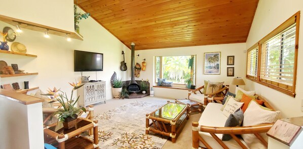 A cozy living room with a wooden ceiling, a fireplace, a TV, and comfortable seating. -  Experience Aloha *Hawaiian Style Hale* (Pahoa)