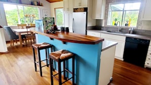 Une cuisine avec un plancher en bois, un îlot central bleu avec des tabourets, des armoires blanches et un réfrigérateur.