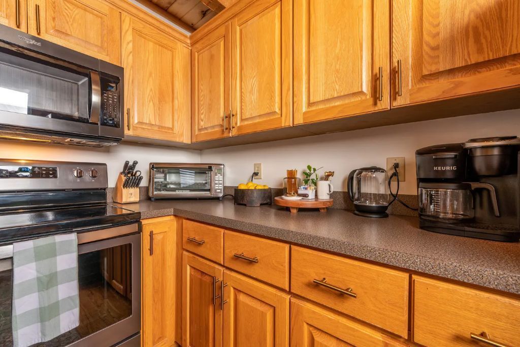 A kitchen with wooden cabinets, a microwave, a toaster, a coffee maker, and a kettle.