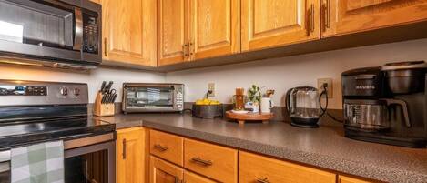 A kitchen with wooden cabinets, a microwave, a toaster, a coffee maker, and a kettle.