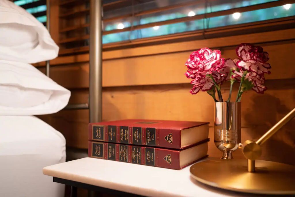 A bookshelf with three red books and a vase with pink flowers.