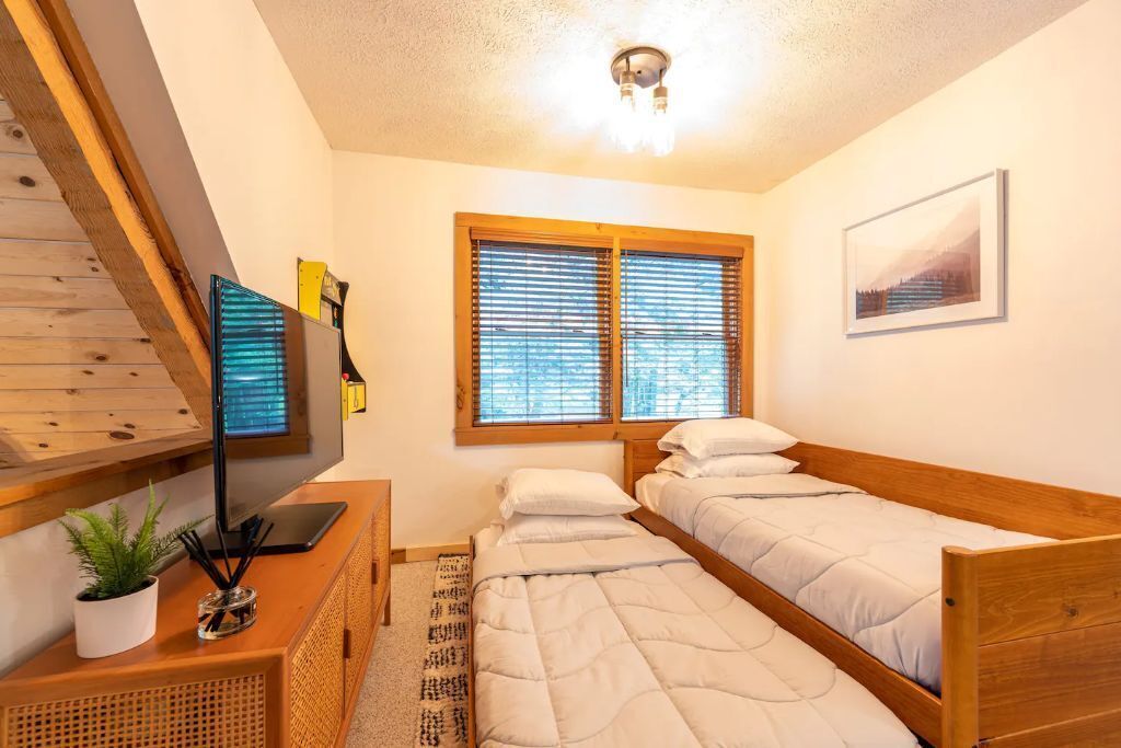 Una camera da letto con due letti singoli, una scrivania con un computer, una televisione e una finestra con tende.