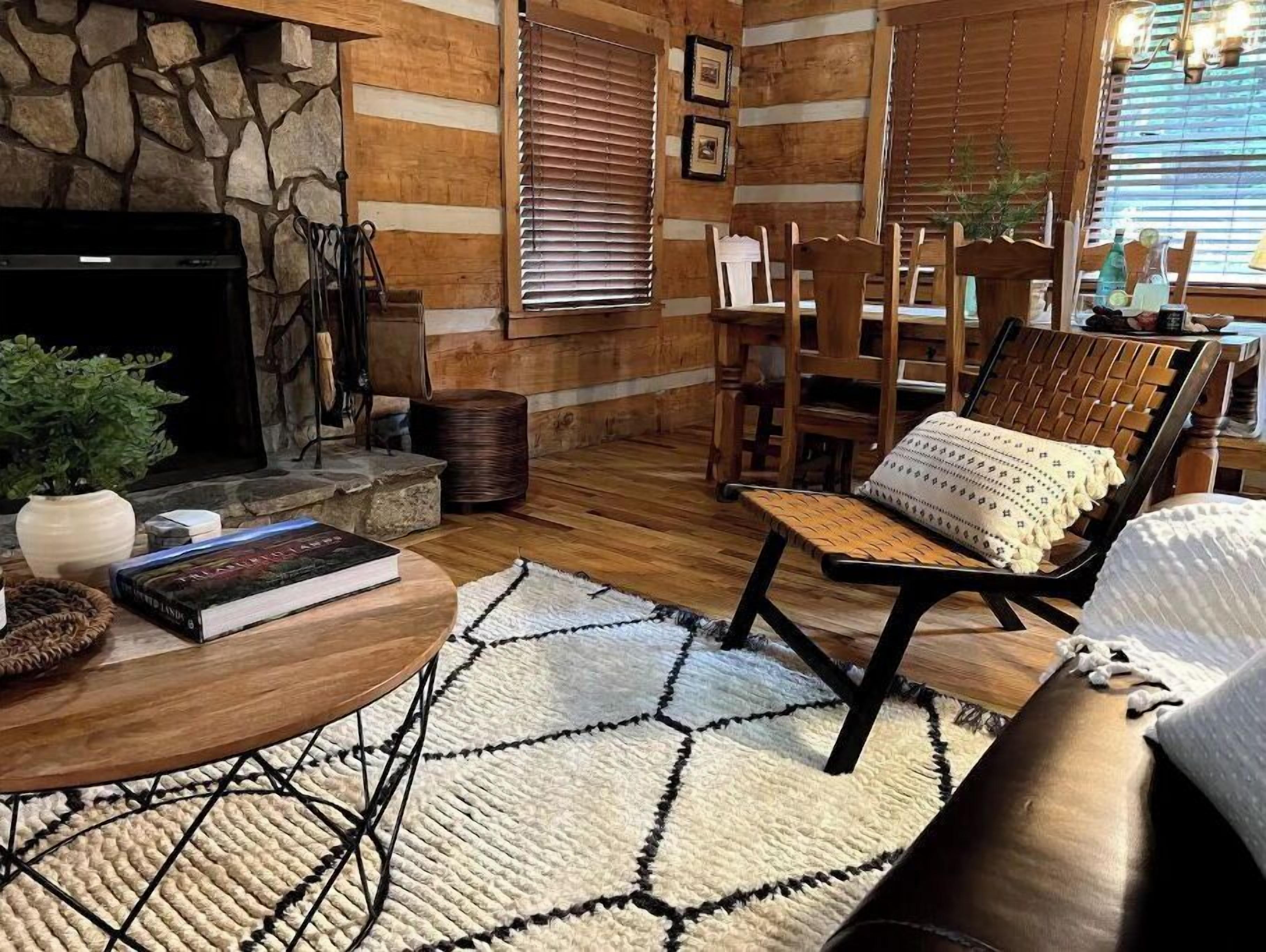 A cozy living room with a stone fireplace, wooden walls, and a comfortable seating area with a round coffee table and a cushioned chair.