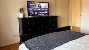A bedroom with a bed, a TV on a black dresser, and a potted plant. - Charming City Home with Professional WFH Setup & AC (Bellevue)