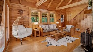 Acogedor interior de una cabaña de madera con sofá, sillones, una mesa de centro y chimenea.