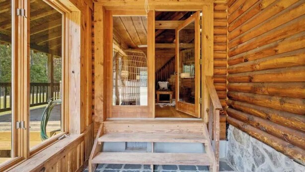 Una cabaña de madera con un porche de baldosas de piedra y vistas al bosque circundante.