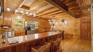 Interior de una cabaña de madera con cocina, comedor y barra.