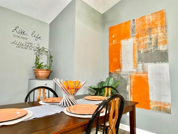 Un coin repas avec une table dressée pour quatre personnes, une plante en pot et une citation inspirante affichée sur le mur.