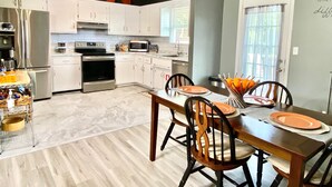 A modern kitchen with white cabinets, stainless steel appliances, and a dining area with a wooden table and chairs.