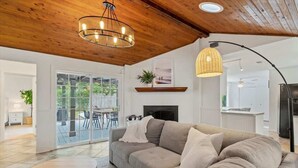 A modern living room with a sectional sofa, a round coffee table, and a fireplace. There is a large window offering a view of the outdoors. - Pool Home with Game Room in Heart of Jax Beach! (Jacksonville Beach)