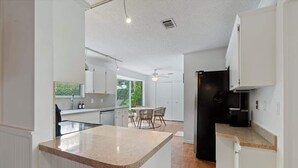 Uma cozinha moderna com armários brancos, bancada de granito e um espaço de refeições com mesa e cadeiras.