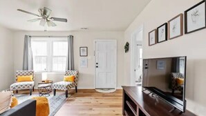 Ein Wohnzimmer mit Deckenventilator, zwei gemusterten Sessel, einem Fernseher und Holzboden.