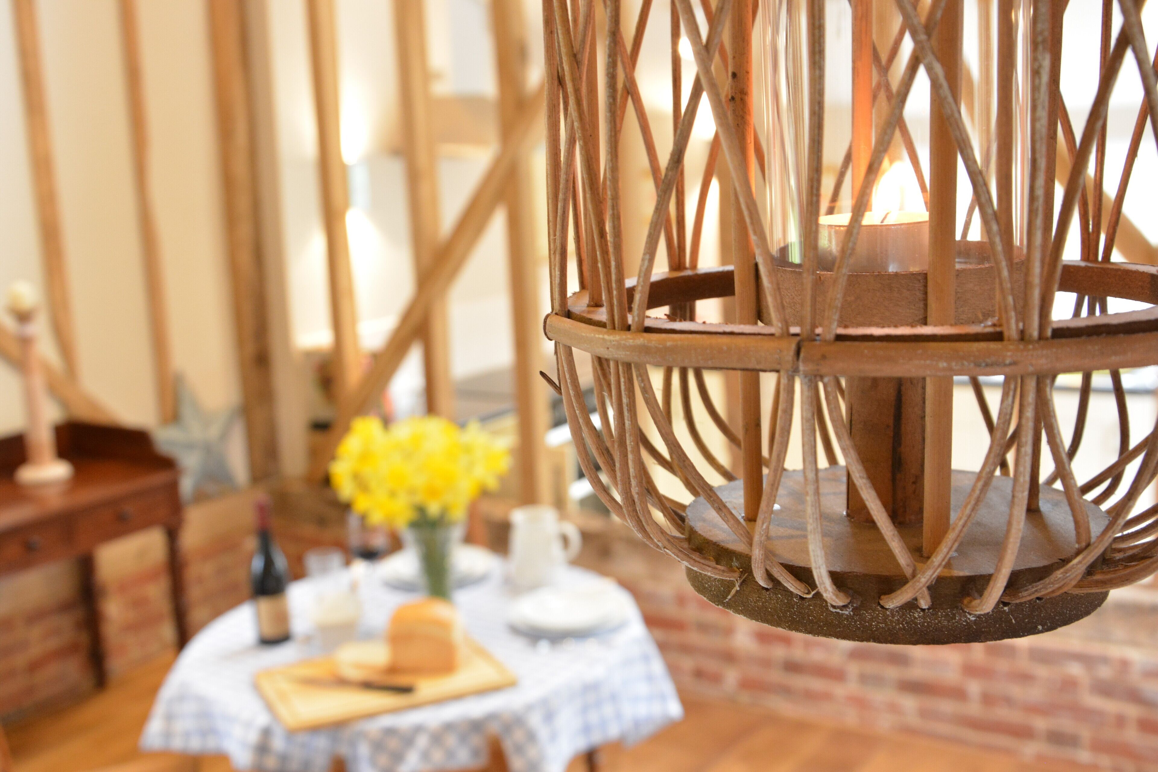 A rustic dining area with a round wooden table, a vase of yellow flowers, and a candle in a woven metal lantern.