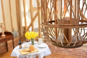 Un coin repas rustique avec une table ronde en bois, un vase rempli de fleurs jaunes et une bougie dans une lanterne en métal tressé.
