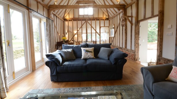 A room with a dark blue sofa, wooden beams on the ceiling, and large windows. - Bird Cottage, Burgh (Woodbridge)