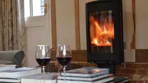 A cozy room with a fireplace, books, and glasses of wine on a table. - Bird Cottage, Burgh (Woodbridge)