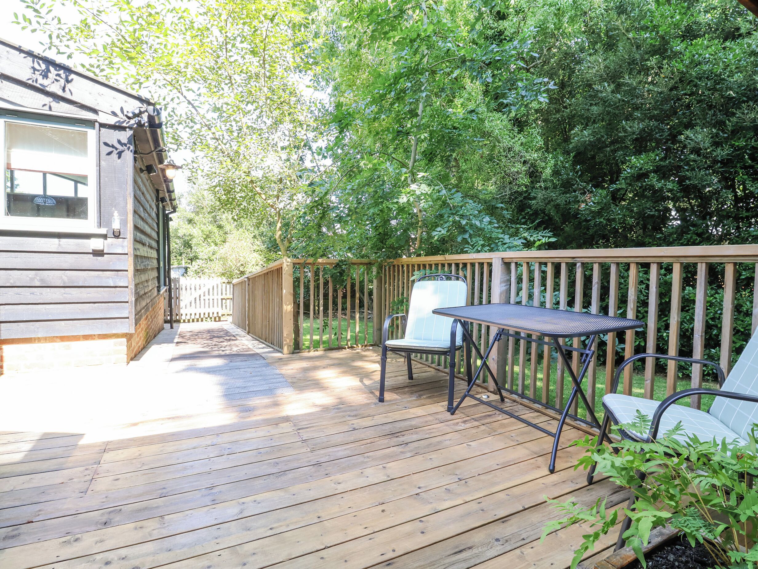 A wooden deck with a table and chairs, surrounded by greenery.