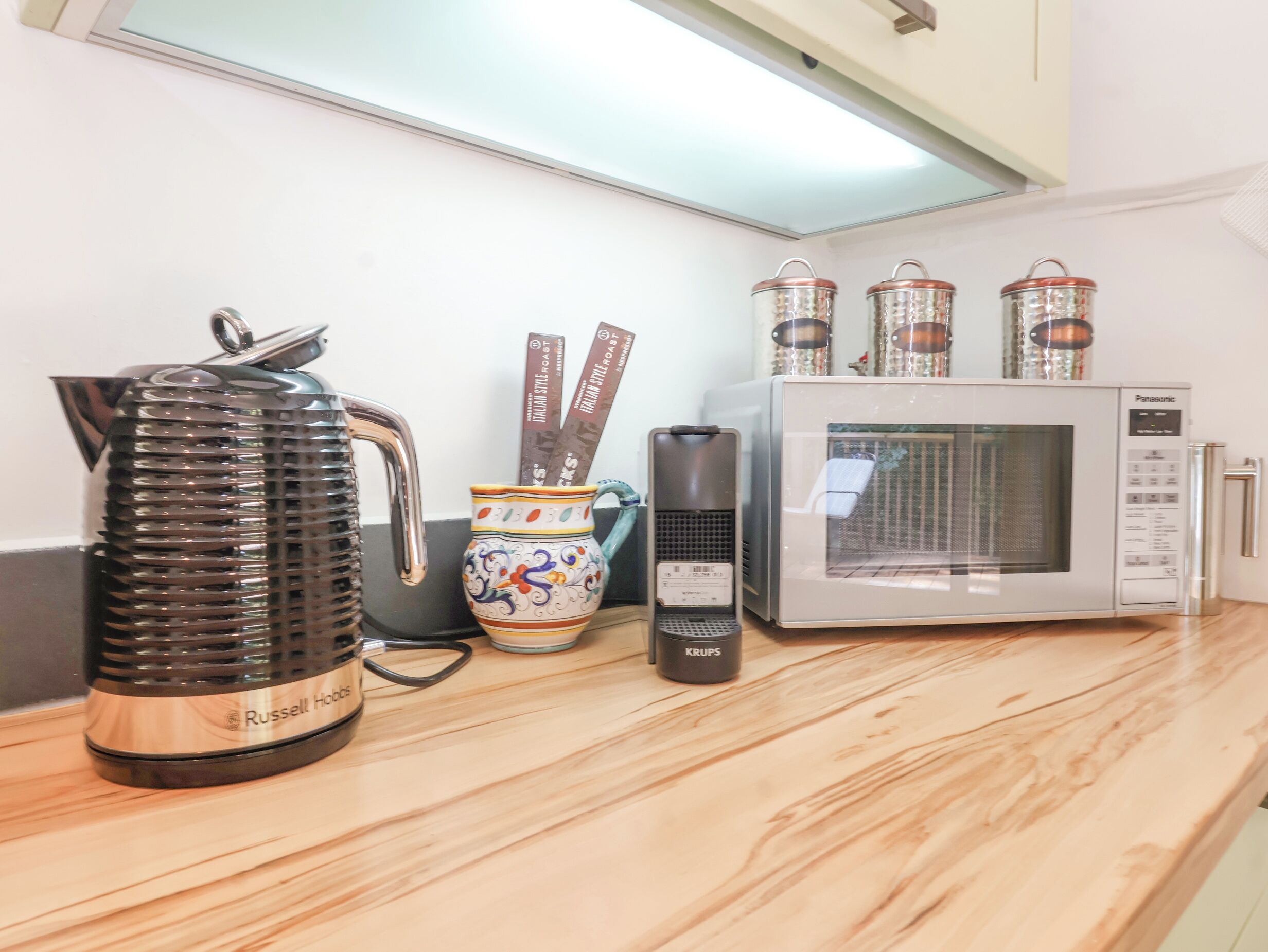 A kitchen counter with a kettle, a microwave, a coffee maker, and a mug.