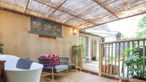 A wooden deck with a cushioned seating area, a glass door leading to a covered patio, and a wooden railing.