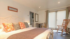 A bedroom with a bed, pillows, a chair, a table, and a window with blinds.