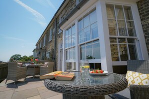 Une terrasse avec des meubles en osier, une table en verre et un livre.