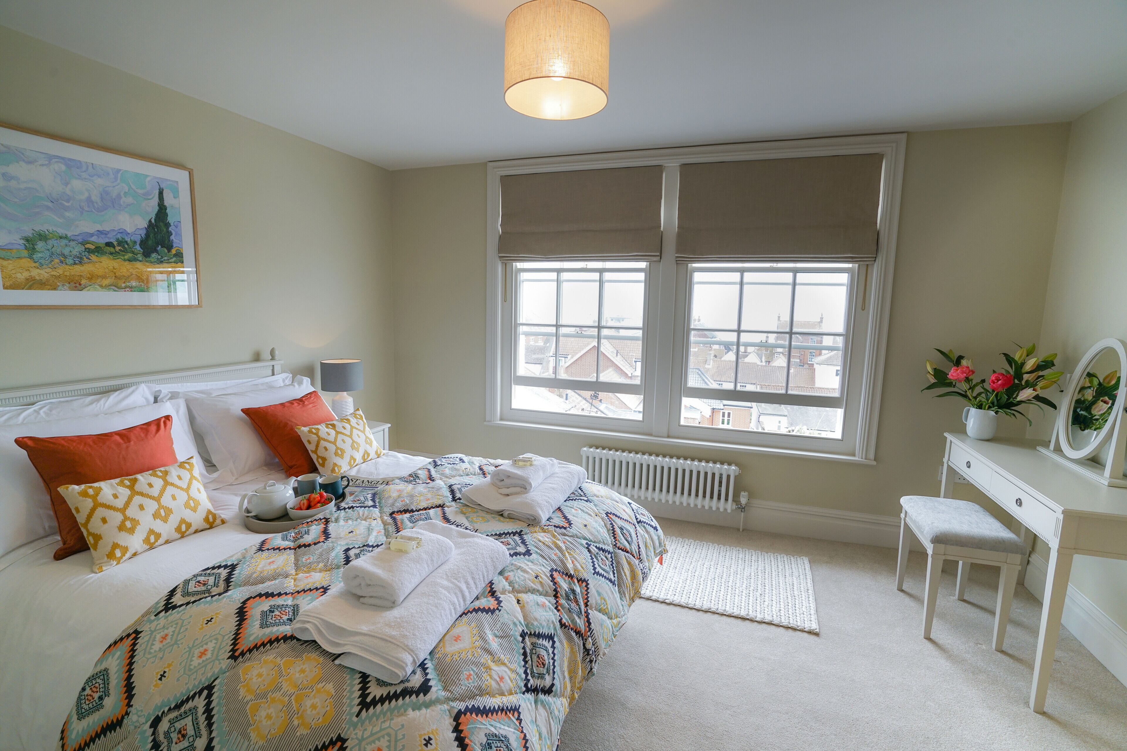 A bedroom with a large bed, a dresser, a window with blinds, and a painting on the wall.