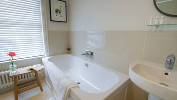 A modern bathroom with a large bathtub, a white sink, and a small stool with a towel.