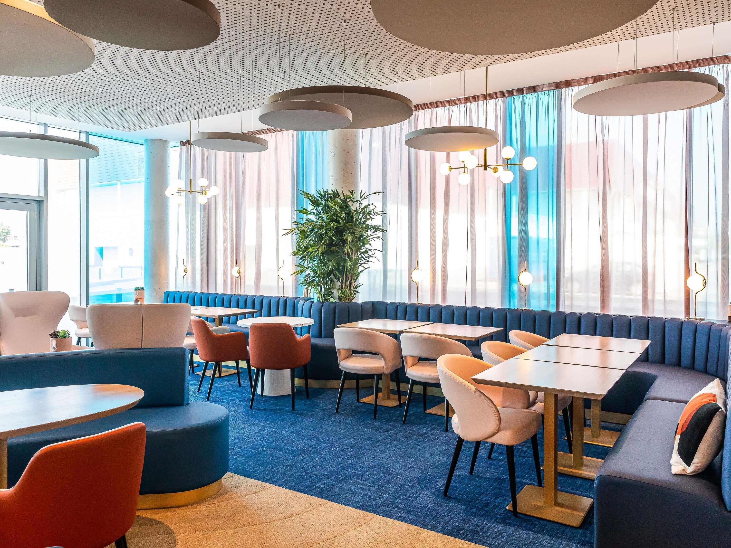 Un intérieur moderne avec des espaces aménagés pour s’asseoir, des tables et une grande fenêtre agrémentée de rideaux.