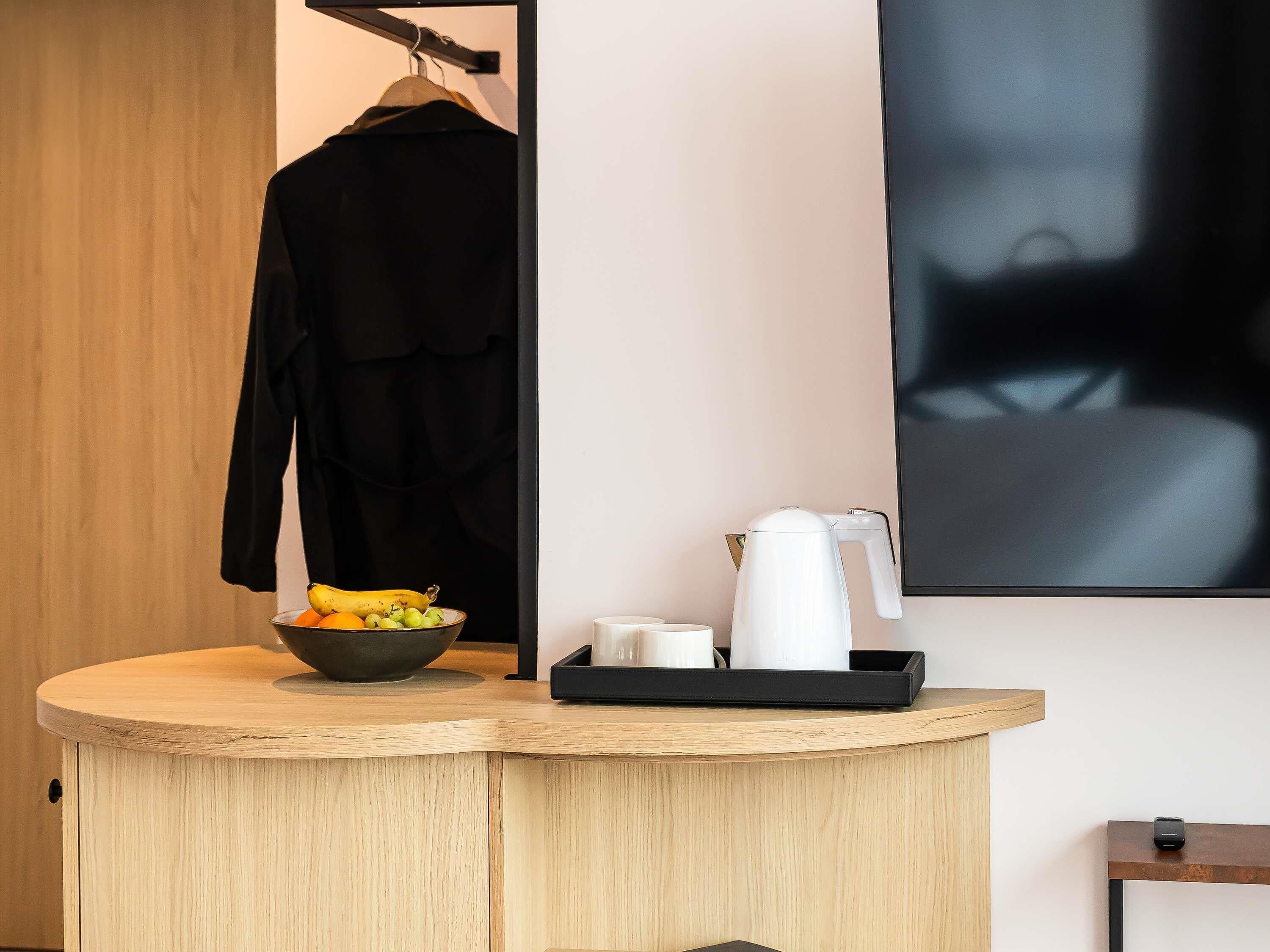 A wooden counter with a bowl of fruit, a white kettle, and a tray with cups.
