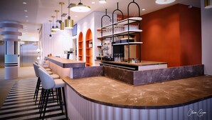 Un área de bar moderna con una barra curva de mármol, varios taburetes y una estantería con cristalería.