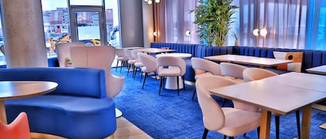 A modern restaurant with blue and white seating, large windows, and a view of the cityscape.