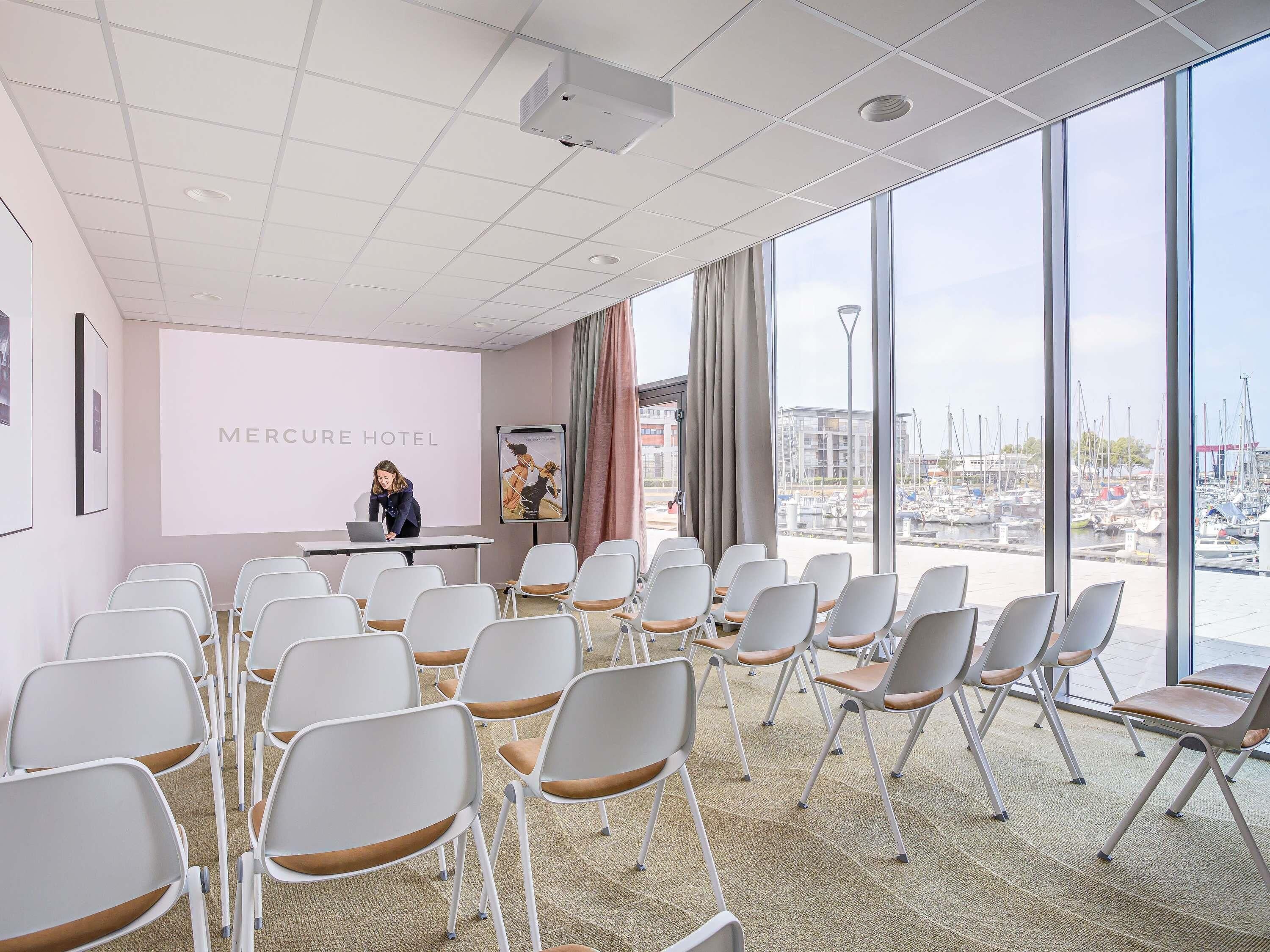 Een vergaderzaal met uitzicht op een jachthaven, een projectiescherm en een presentatiegedeelte.