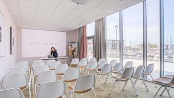 Een vergaderzaal met uitzicht op een jachthaven, een projectiescherm en een presentatiegedeelte.