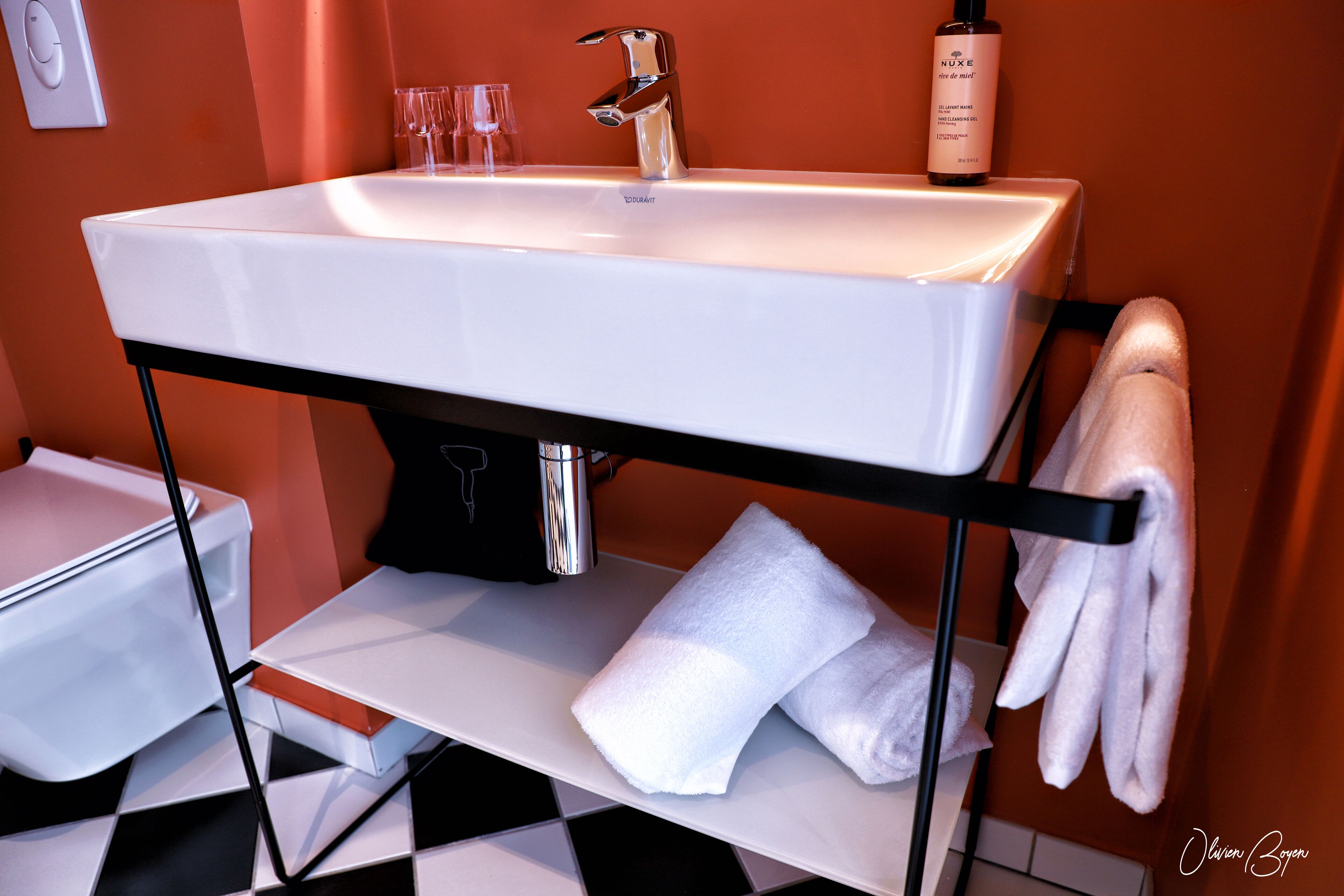 Un baño moderno con un lavamanos blanco, un perchero y una botella de champú.
