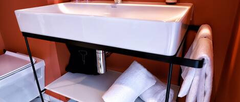 A modern bathroom with a white sink, a towel rack, and a bottle of shampoo.