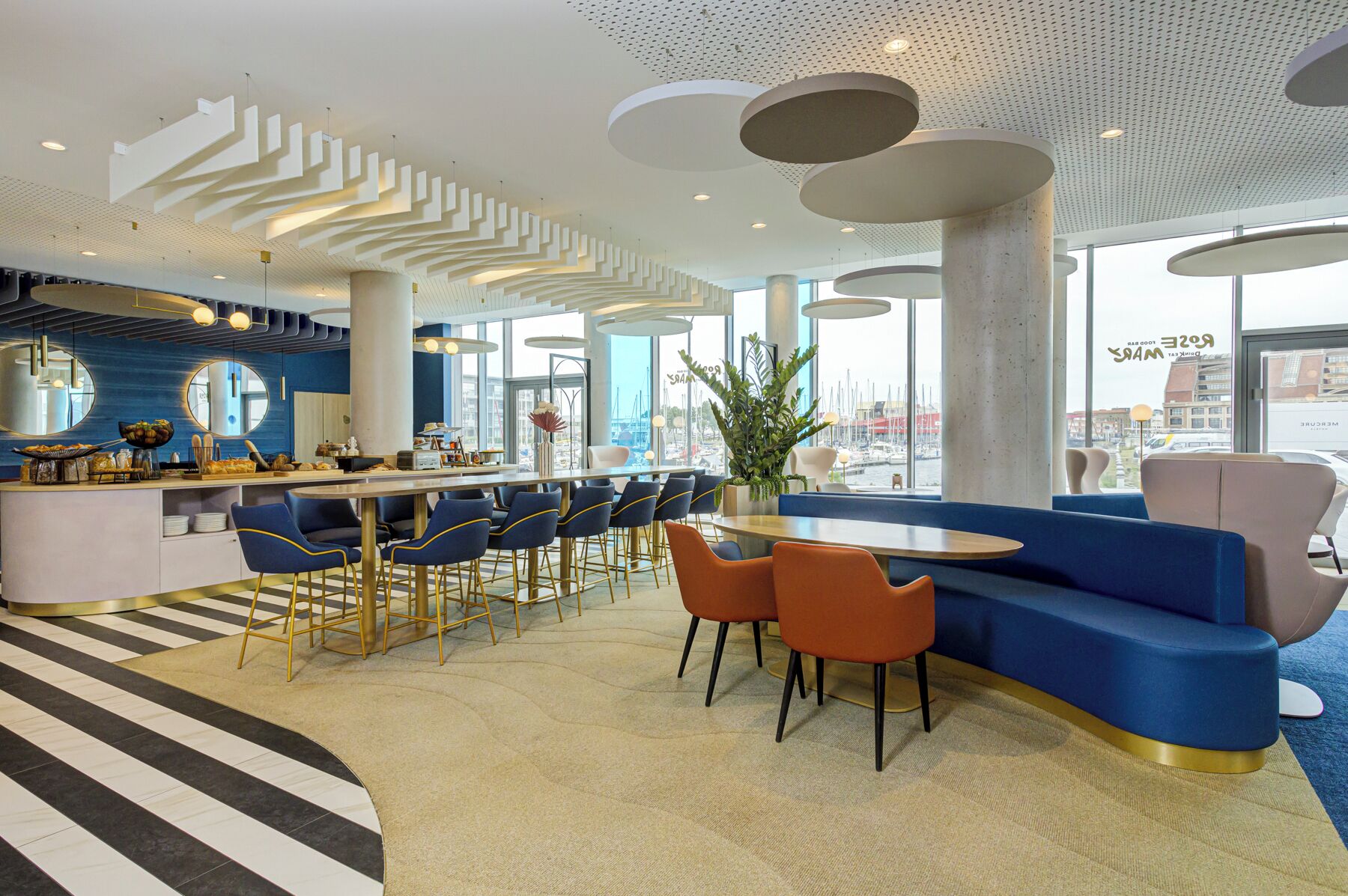 A modern restaurant with a bar area, seating, and large windows offering a view of the harbor.