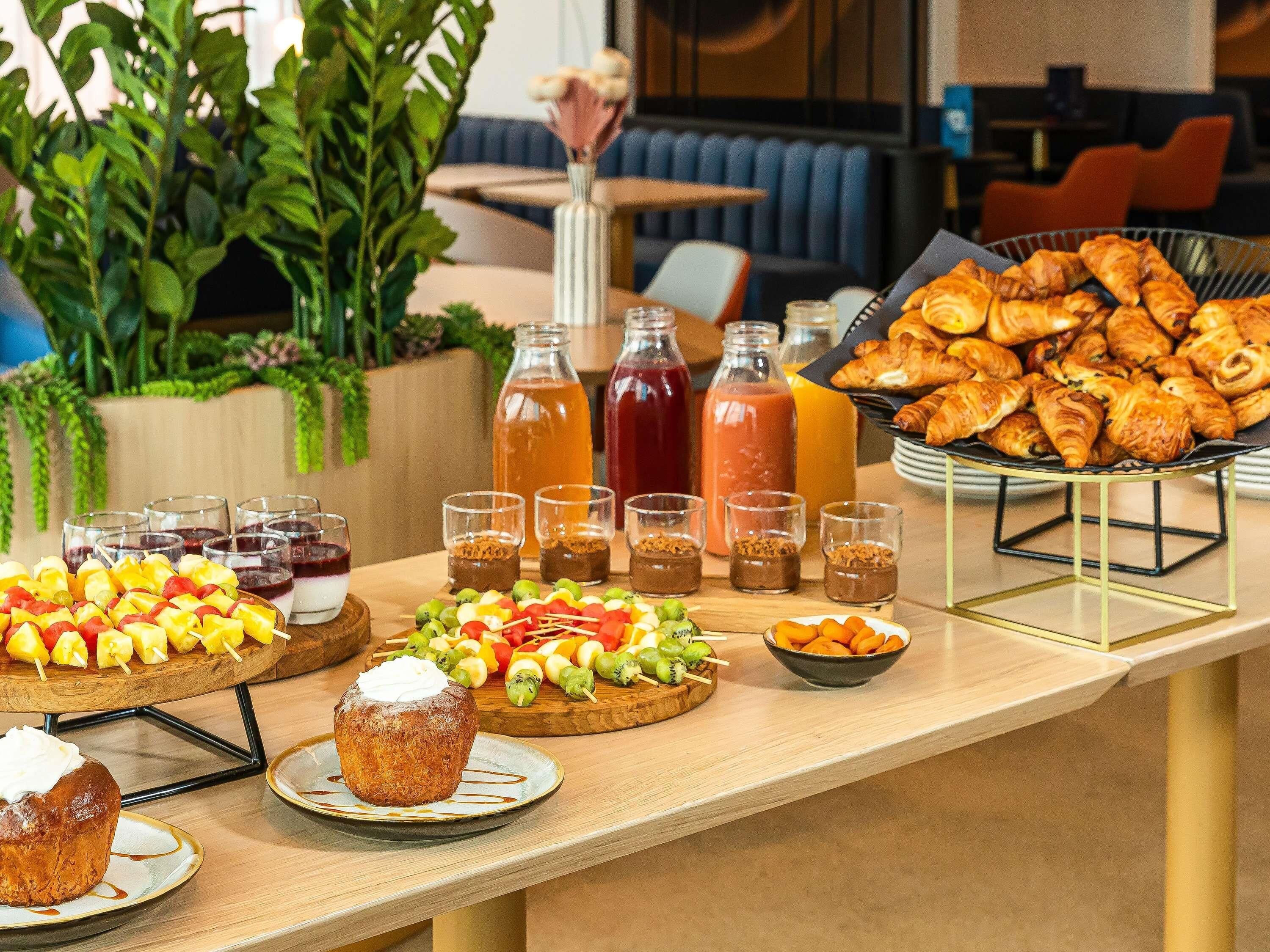 A buffet table with various food items, including pastries, fruit skewers, and beverages.