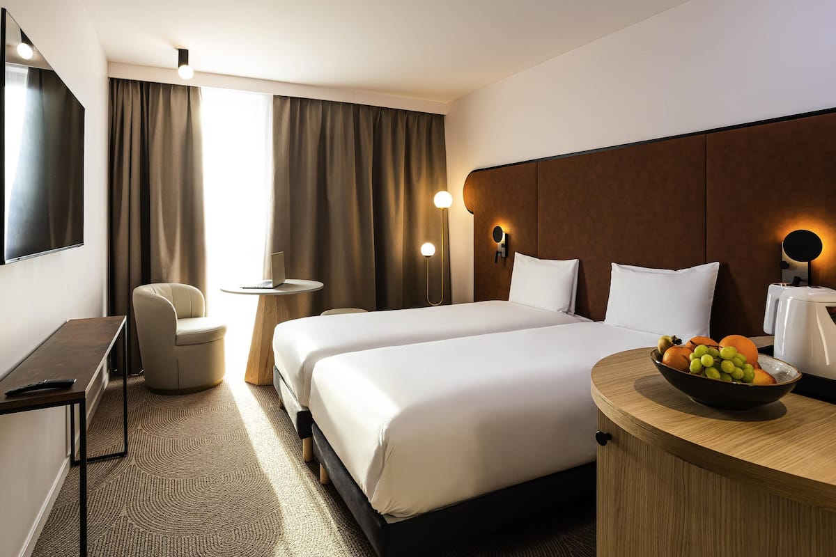 Ein Hotelzimmer mit Bett, Nachttisch, Stuhl, Schreibtisch und einer Obstschale.