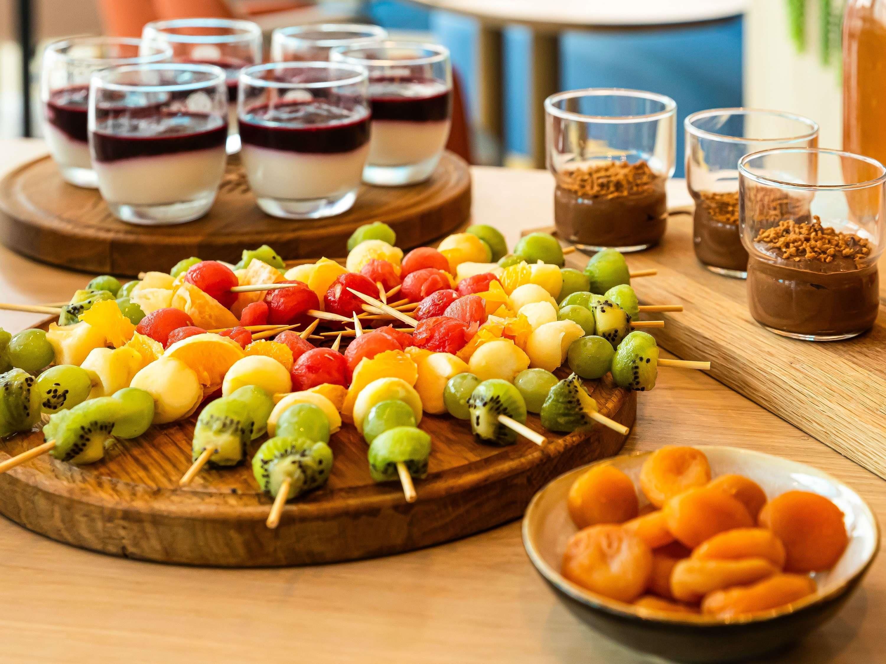 A wooden board with fruit skewers and a bowl of apricots.