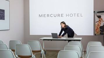 A conference room with a projection screen displaying 'MERCURE HOTEL' and a person using a laptop.