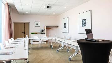 Una sala de conferencias con una mesa blanca, sillas, un proyector y fotografías enmarcadas en la pared.