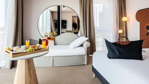 Habitación de hotel con cama, una mesita con desayuno, espejo y vista a la ciudad.