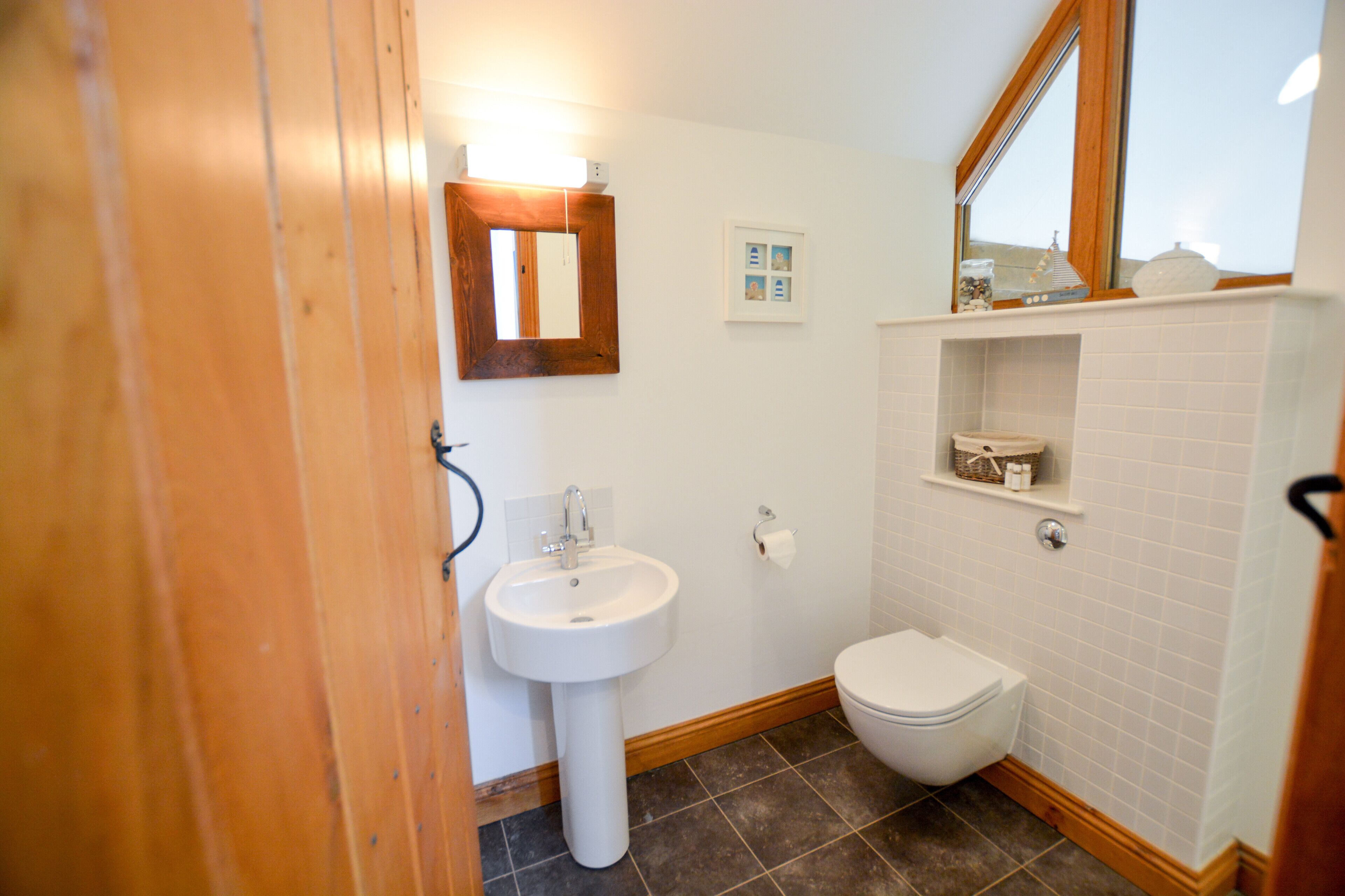 A bathroom with a white sink, a toilet, and a mirror. There is a shelf above the toilet with a small decorative item.