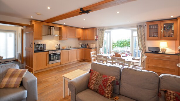 A spacious living area with a sofa, a dining table, and a kitchen in the background. - Three Chantry Barns, Orford (Woodbridge)