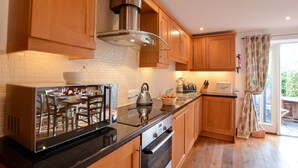 A modern kitchen with wooden cabinets, a stainless steel range hood, a built-in oven, and a large window with curtains. - Three Chantry Barns, Orford (Woodbridge)