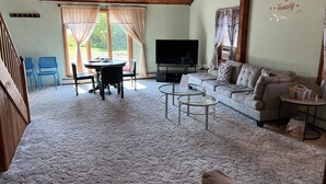 A living room with a sofa, a TV, a glass coffee table, and a dining area with chairs and a table. - High Peaks Haven is in the heart of Adirondack. Come enjoy with famil (Keeseville)