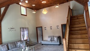 A spacious loft with a high ceiling, exposed wooden beams, a staircase, a sofa, a coffee table, and a chandelier. - High Peaks Haven is in the heart of Adirondack. Come enjoy with famil (Keeseville)