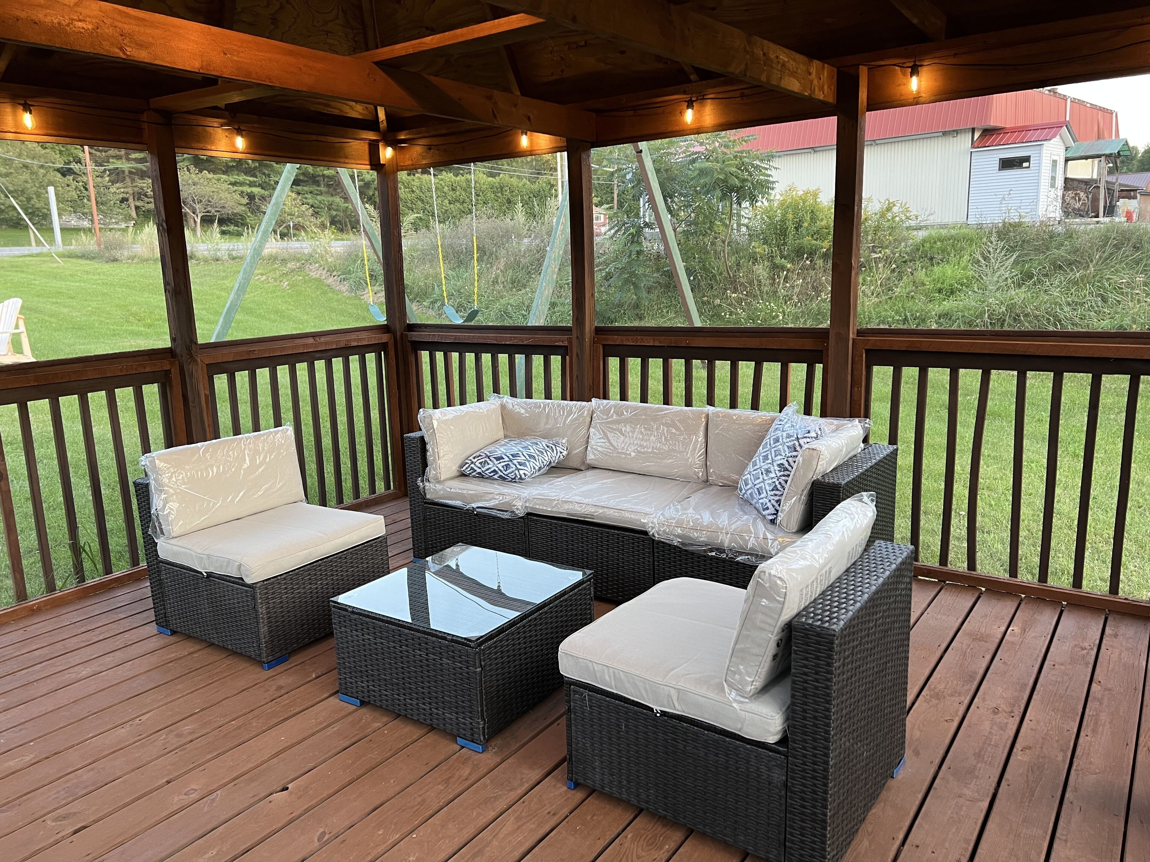 A covered outdoor seating area with wicker furniture and a glass coffee table.