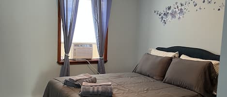 A bedroom with a bed, curtains, a wall decoration, and a ceiling light.