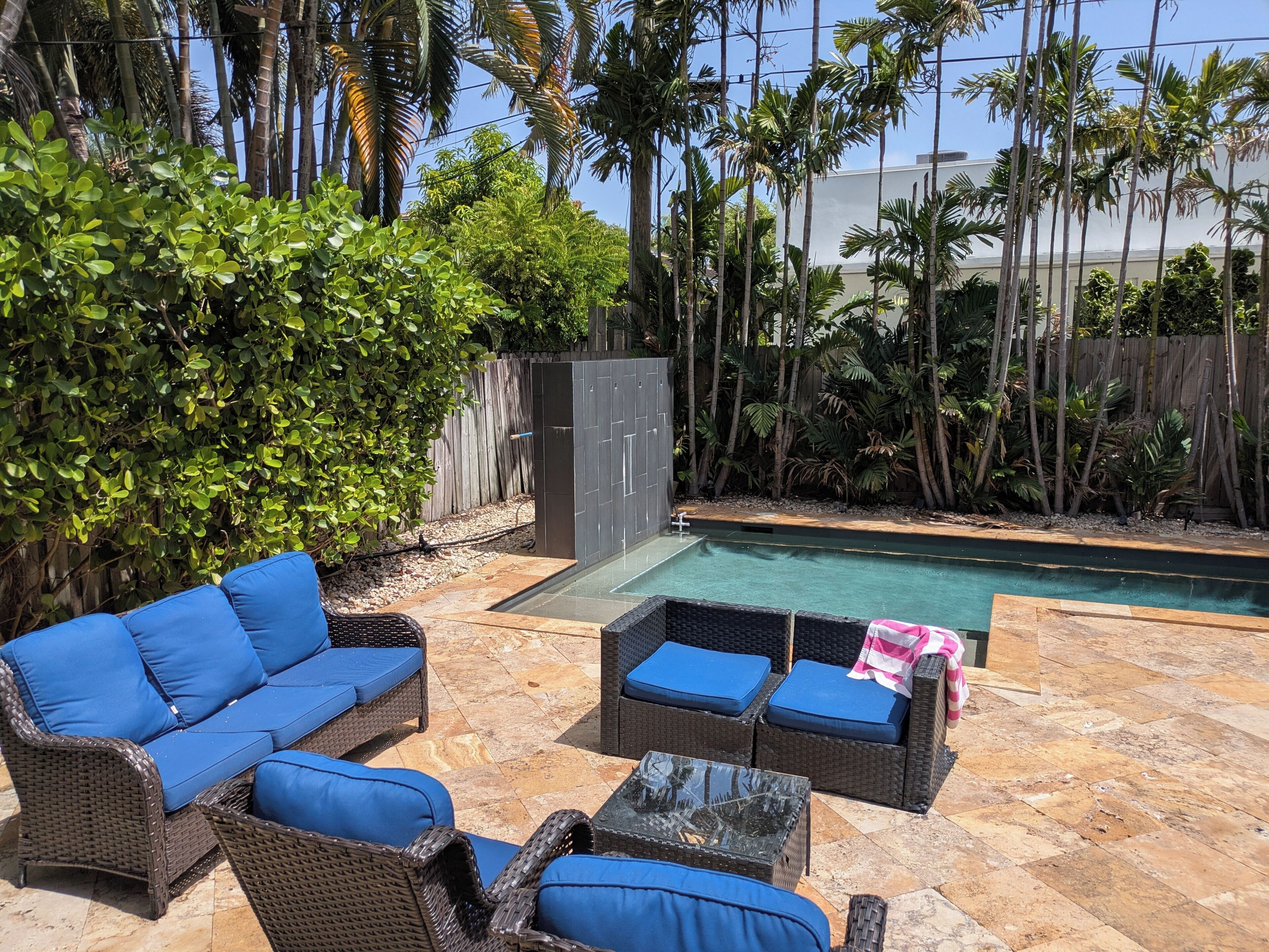 Un espace aménagé au bord de la piscine, avec des meubles en osier, une piscine et des plantes tropicales.